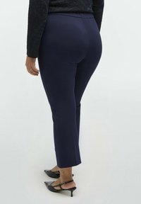 Marinblå elastiska byxor med slim fit, midjehöjd och beskuren längd. Matchas med svarta spetsiga klackskor.