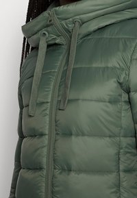 Giacca verde imbottita con cappuccio, dotata di zip frontale completa, cordini e texture trapuntata. Finitura in tessuto liscia.