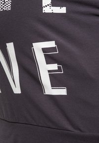 Gros plan d’un tissu foncé avec de grandes lettres blanches stylisées « N » et « E » imprimées, montrant la texture et de légers plis sur le matériau.