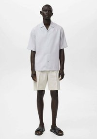 Lysegrå kortærmet skjorte med afslappet krave, knaplukning fortil, parret med beige shorts og sorte sandaler. Glat stofstruktur.