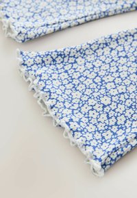 Textília kék-fehér virágmintával. A szövet fodros széllel és sima textúrával rendelkezik, a minta közelről látható.