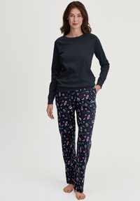 Een navy blauwe long-sleeve top gecombineerd met gestreepte pyjamabroek met een donkere achtergrond en feestelijke motieven in rood, wit en groen.