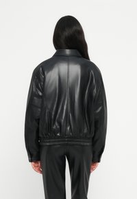 Veste en cuir noir avec une coupe relaxée, dotée d'un col et d'une taille élastique. Texture lisse, détails minimaux.