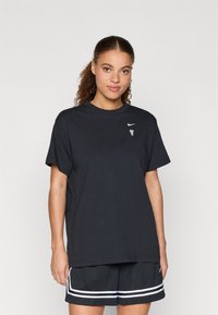 Μαύρο βαμβακερό T-shirt με χαλαρή εφαρμογή, στρογγυλή λαιμόκοψη, κοντά μανίκια και λευκό λογότυπο Nike στο στήθος. Συνδυασμένο με μαύρη αθλητική βερμούδα με λευκές ρίγες.