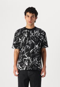 Black T-shirt featuring a bold, abstract white print. Short sleeves, round neckline, made from a textured fabric. Casual fit.