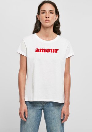 Fehér pamut póló rövid ujjal és kerek nyakkivágással. A frontrészen hangsúlyosan megjelenik a piros színű "amour" felirat.