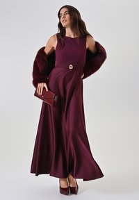 Robe de soirée bourgogne avec un corsage ajusté, une jupe évasée et un bouton décoratif en or à la taille. Assortie à un écharpe en fausse fourrure et à une pochette assortie.