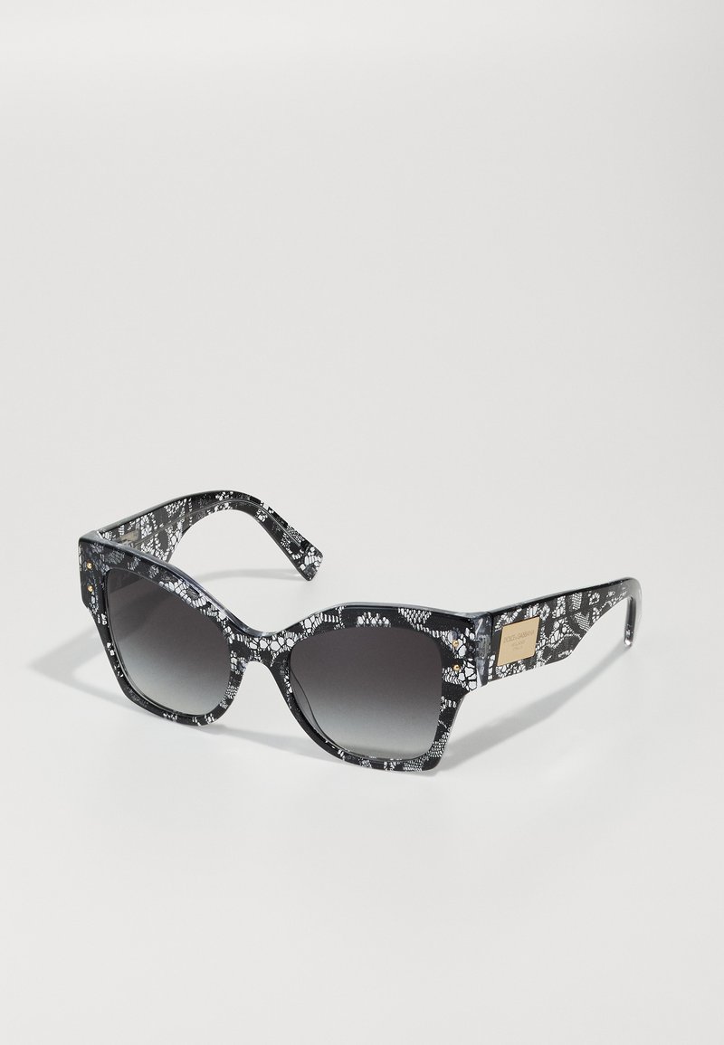 Sunglasses with a black and white lace-patterned frame, angular shape, gradient gray lenses, and gold-toned hardware detail.