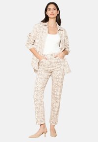 Ensemble imprimé serpent beige avec une chemise à boutons et un pantalon ajusté, fabriqué en tissu lisse, associé à des talons nus.