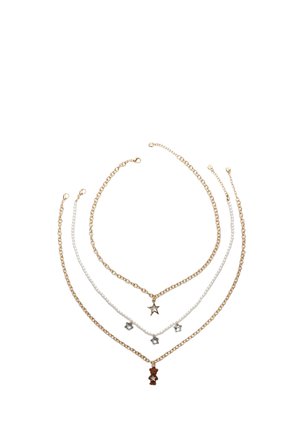 Ensemble de colliers superposés comprenant des chaînes en métal doré et argenté, avec des charms en forme d'étoile et géométriques, et un pendentif en forme d'ourson en gélatine.