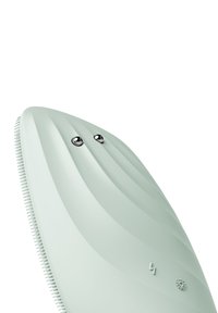 Siliconansiktsrengöringsapparat i matt mintgrön. Har rundad form, räfflad yta, två silverknappar och logotypdetaljer.