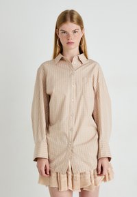 Beige en lichtoranje geruit shirt met lange mouwen, knoopsluiting aan de voorkant en een borstzak, gecombineerd met een gerimpelde, licht beige gelaagde rok.