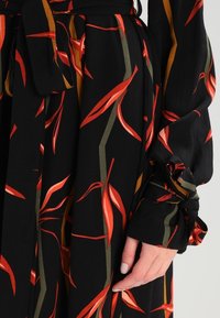 Schwarzes Kleid mit Rot- und Orangetönen Blattmuster; lange Ärmel mit gebundenen Manschetten. Weicher, leichter Stoff mit fließendem Design und natürlichem Fall.