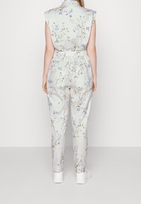 Light grey jumpsuit with a floral pattern, short sleeves, elastic waistband, and tapered legs. Worn with white sneakers.