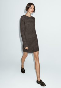 Brown knitted sweater dress featuring a textured ribbed pattern, long sleeves, and a fitted silhouette, paired with dark loafers.