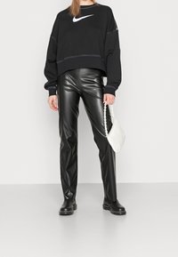 Sudadera negra recortada con logo blanco de Nike, combinada con pantalones de cuero negro brillantes. Los accesorios incluyen un peque ño bolso blanco con una correa de cadena.