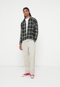 Czarna i biała koszula w kratę na białej koszulce, w połączeniu z jasnobeżowymi spodniami typu wide-leg i czerwonymi sneakersami. Prosta biżuteria i brak wyróżniających się wzorów.