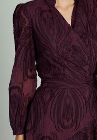 Rochie închisă la culoare, cu un croi din material ușor, având broderie florală texturată, mâneci lungi și o curea la talie. Material ușor cu un finisaj moale și transparent.