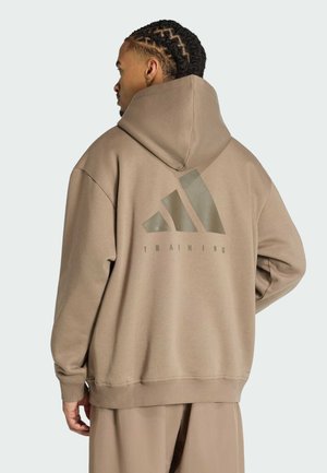 Man with braided hair wearing a beige Adidas Training hoodie, shown from the back against a plain light background.
