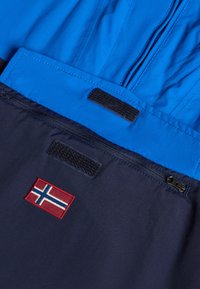 Blauwe en marineblauwe jas met een rits en klittenbandsluiting. Beschikt over een kleine geborduurde Noorse vlag. Gladde textuur, sportief ontwerp.