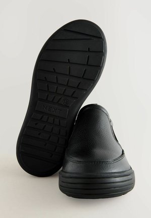 Crne slip-on cipele s gornjim dijelom od teksturirane kože, gumeni potplat s uzorkom za prianjanje i utisnutim logotipom sa strane.
