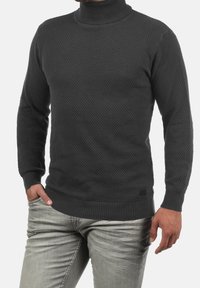 Pull col roulé gris foncé avec un motif en nid d'abeille texturé, poignets et ourlet côtelés. Associé à un jean gris clair.