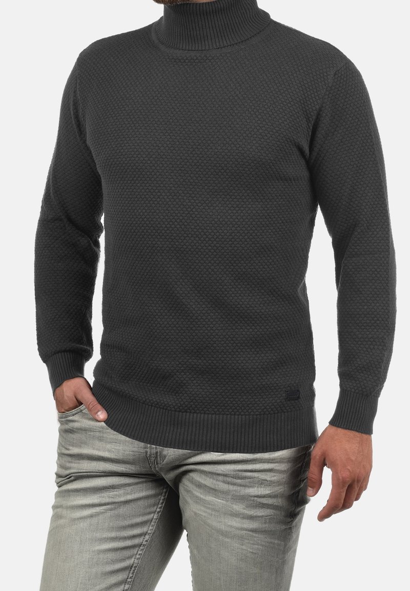 Pull col roulé gris foncé avec un motif en nid d'abeille texturé, poignets et ourlet côtelés. Associé à un jean gris clair.