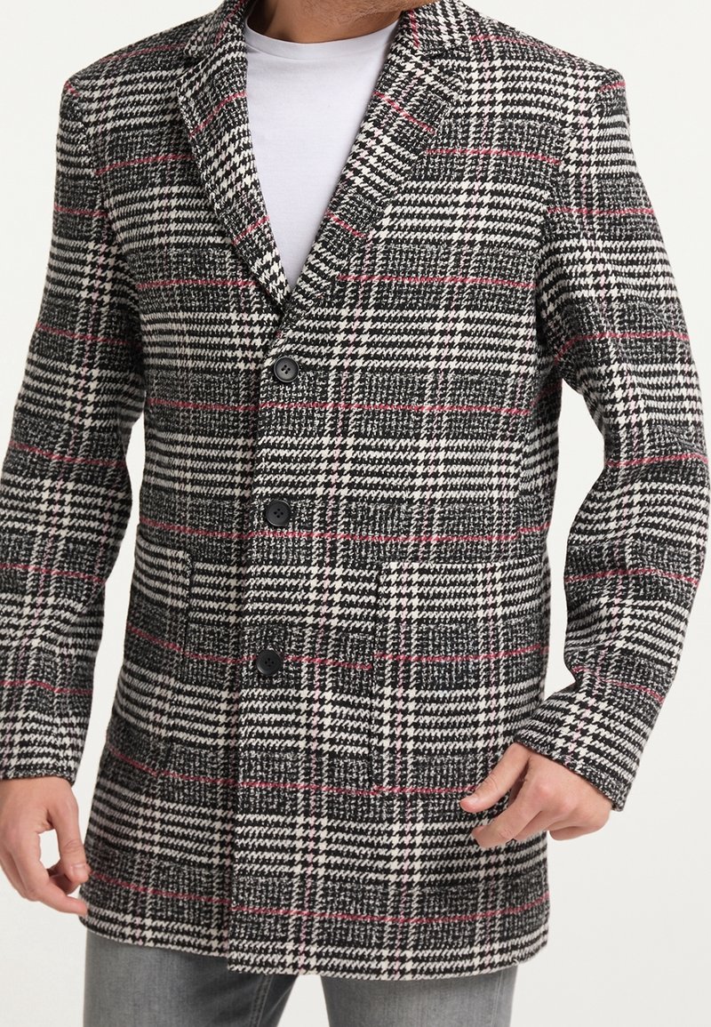 Black and white checkered coat with red accents, featuring a notched lapel, three buttons, and a textured fabric. Includes two side pockets.