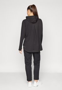 Black hoodie with a loose fit, long sleeves, and a drawstring hood. Worn with matching black tapered pants and white sneakers.