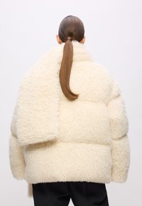 Teksturirana, krema-boje oversized puffer jakna napravljena od pahuljastog materijala, s širokim rukavima i visokim ovratnikom, sa mekanim izgledom.