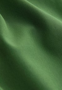 Tissu vert léger avec une texture lisse, présentant une finition mate et une légère brillance. Le matériau semble souple et durable.