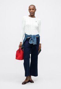 Biały sweter w splot kablowy, dżinsowa kurtka związana w talii, granatowe szerokie spodnie, czerwona torebka o fakturze i burgundowe baleriny.