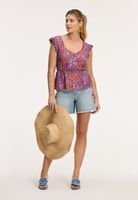 Krāsains ziedu raksta tops ar frēzētiem piedurknēm, kopā ar džinsa šortiem. Modelis tur lielu salmu saulessargu un valkā zilu ziedu raksta slida sandali.