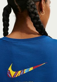 Blå bomulls-t-shirt med en mångfärgad Nike swoosh-logotyp och text nedanför. Halsringningen är ribbad och tyget ser slätt ut.