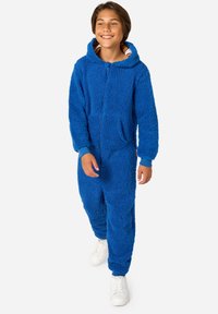 Modra puhasta kombinezona, izdelana iz mehkega, teksturiranega materiala; ima sprednji zadrgo, kapuco in žepke s kontrastnimi manšetami in podlogo.