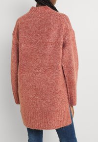 Gebreide cardigan van zachte, textuurstof, met een relaxed fit, hoge nek en geribde zoom. Kleur: warm koraal met subtiele spikkels.