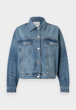 Femme portant une veste en jean claire sur un top blanc, jean bleu clair taille haute avec ourlets bruts, ceinture noire et sandales à talons noires ouvertes à l'avant.