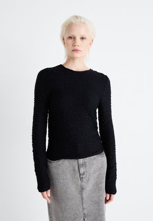 Svart langermet topp med en teksturert, rynket design. Har rund hals og smal passform, sammen med et grått denimskjørt.