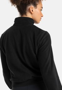 Black fleece pullover jacket with a high collar, textured surface, and elasticized hem. Features long sleeves and a snug fit.