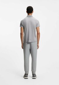 Mand stående med ryggen til iført en lysegrå polo med korte ærmer, grå joggingbukser og grå sneakers med hvide såler.