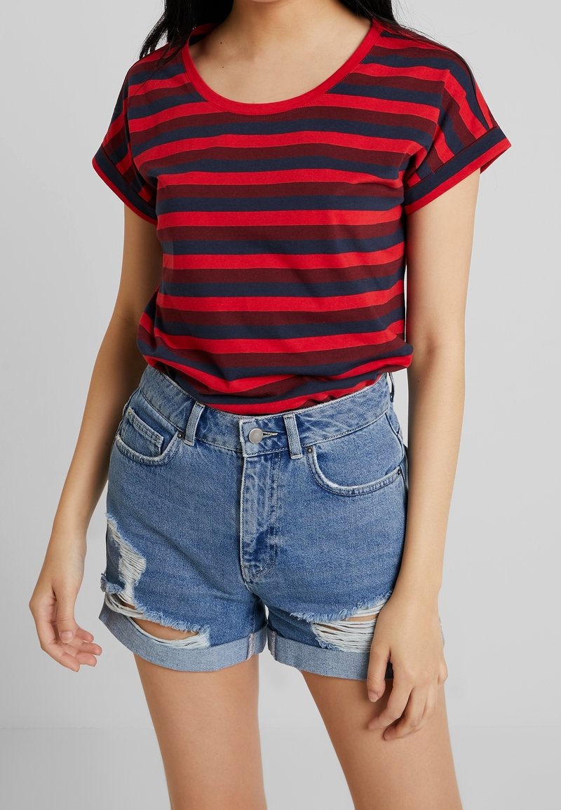 Personne portant un t-shirt à manches courtes rayé rouge et bleu marine, rentré dans un short en jean taille haute usé avec un ourlet retroussé.