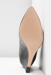 Chaussure à talon haut noire à bout pointu en cuir texturé avec semelle lisse, taille 37, marquée "Made in Spain" sur la semelle.