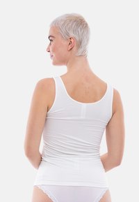 White tank top made of lightweight, smooth fabric, featuring a round neckline and thin straps, fitted shape, and curved hemline.