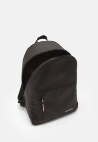 Zaino nero con forma arrotondata, realizzato in materiale testurizzato. Presenta una tasca frontale con zip e dettagli colorati, e una maniglia superiore per il trasporto.