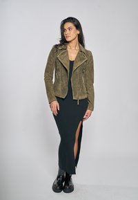 Olivgrön mockacykeljacka med dragkedjefickor, bärs över en svart ribbad klänning med sidospjälka, kombinerad med svarta platåboots.