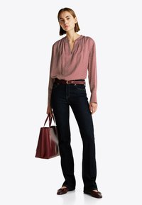 Rød og hvid prikket bluse med draperet halsudskæring, parret med mørke flared jeans og en bordaux tote bag. Brune flade sko fuldender looket.