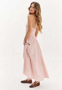 Svetloružová maxi šaty s tenkými ramienkami, na gumičku v páse a s rozšírenou sukňou. V kombinácii s balerínkami s leopardím vzorom. Hladká textúra látky.