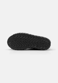 Suela de zapato deportivo negra con un patrón de tracción texturizado que presenta formas en zigzag y onduladas para ofrecer agarre y estabilidad. Material de goma duradera.