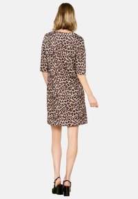 Kleid mit Leopardenmuster, kurzen Ärmeln, lockerer Passform, Rundhalsausschnitt, weichem Material und knielanger Länge, getragen mit klobigen schwarzen Absätzen.