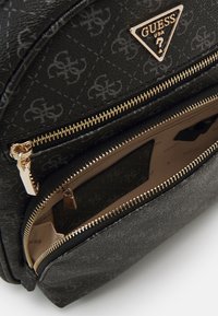 Mochila negra texturizada con herrajes dorados, que cuenta con compartimentos con doble cremallera y una placa con el logo en la parte delantera.